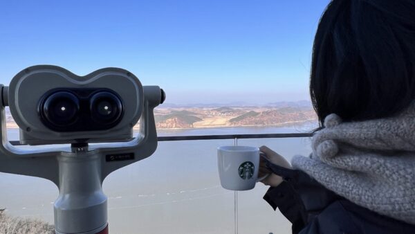 A woman holding a cup of Starbucks Coffee while getting a close up view of North Korean from Aegibong Peak Observatory
