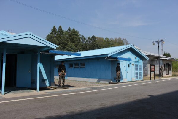 The blue UNC buildings including the UNC Military Armistice Commission Conference Room straddling the Military Demarcation Line with South Korean border guards standing in front