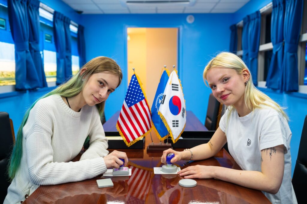 Two women inside the UNCMAC blue conference room at the JSA Museum stamping cards
